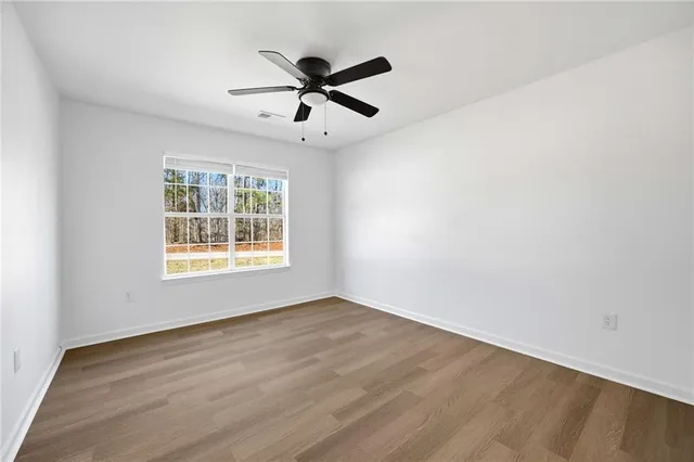 an empty room with wooden floor fan and windows