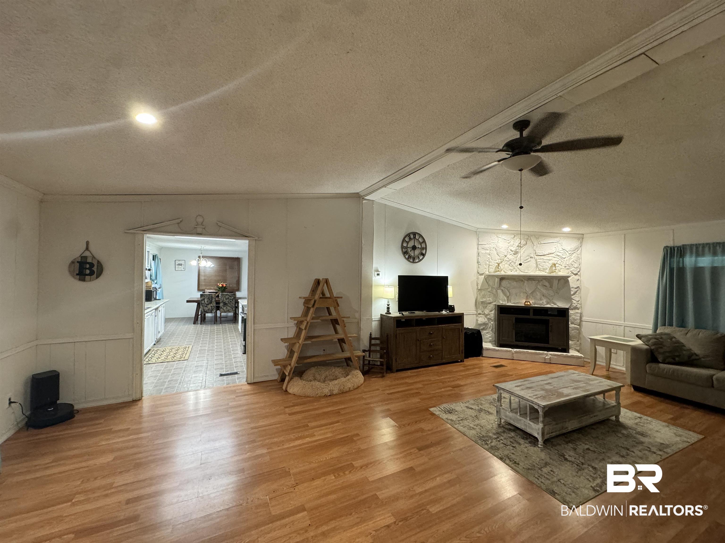 51235 Phillipsville Road Bay Minette, AL 36507 - Photo 23 of 63 Living area with a decorative wall, a ceiling fan, a stone fireplace, wood finished floors, and ornamental molding