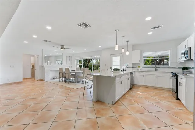 a large white kitchen with kitchen island a sink a counter top stainless steel appliances and cabinets