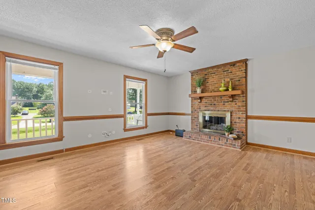 a view of a livingroom with a fireplace a ceiling fan and windows