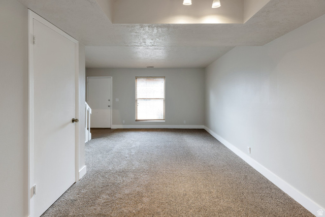 88 West 50 South, Unit J10 Centerville, UT 84014 - Photo 4 of 19 Spacious room featuring neutral carpeting, light gray walls, a window with blinds, white baseboards, and a dropped ceiling section with recessed lighting