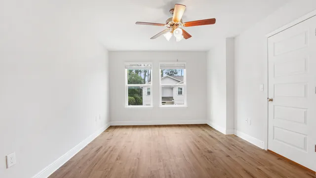 an empty room with wooden floor fan and windows