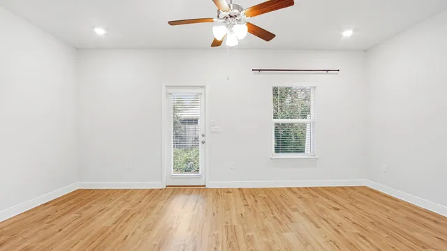 an empty room with wooden floor chandelier fan and windows