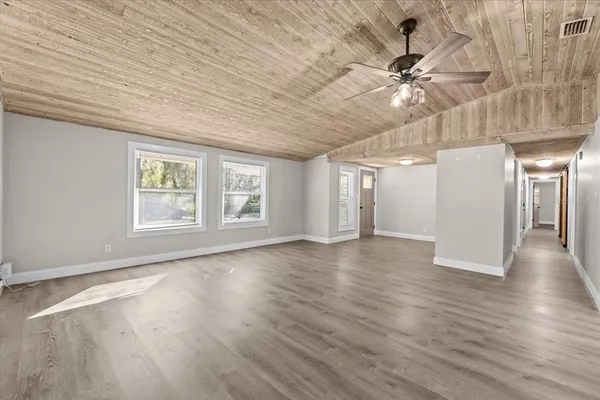 an empty room with wooden floor fan and windows