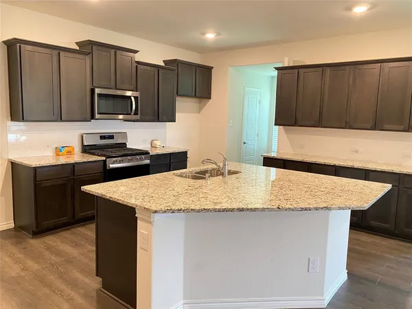 a kitchen with stainless steel appliances granite countertop a sink dishwasher a stove top oven a refrigerator with grey cabinets and wooden floor