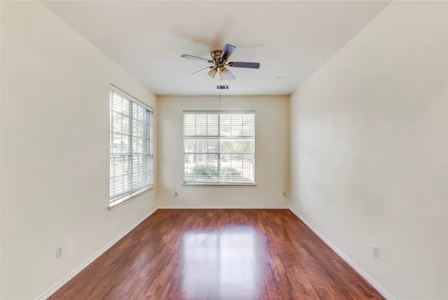 an empty room with wooden floor chandelier fan and windows