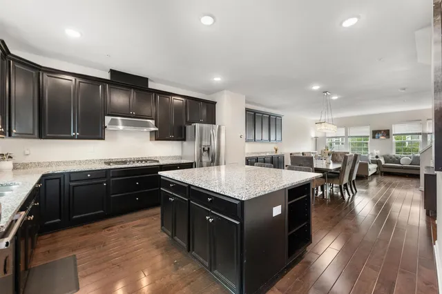 a kitchen with stainless steel appliances granite countertop wooden cabinets a sink dishwasher a stove and a refrigerator with wooden floor