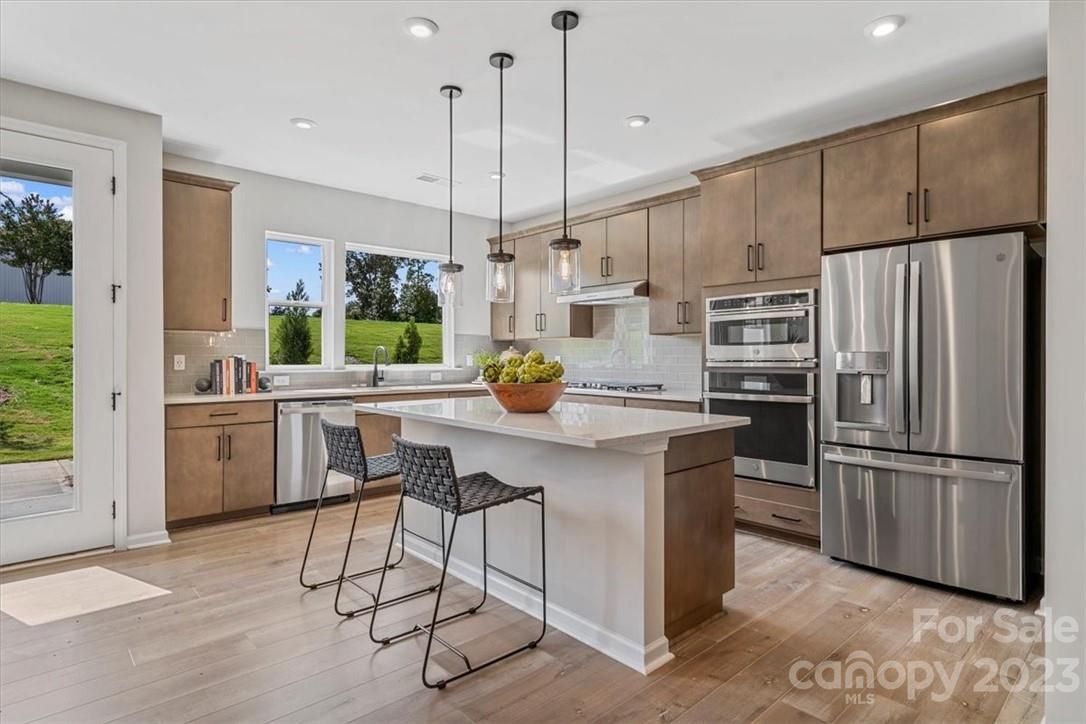a kitchen with stainless steel appliances kitchen island granite countertop a refrigerator a oven a sink a dining table and chairs with wooden floor