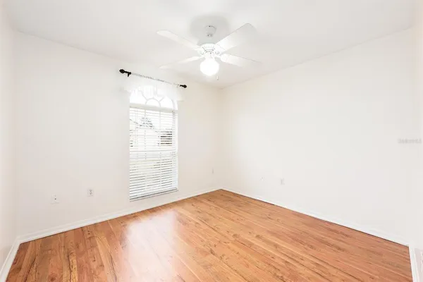 an empty room with wooden floor fan and windows