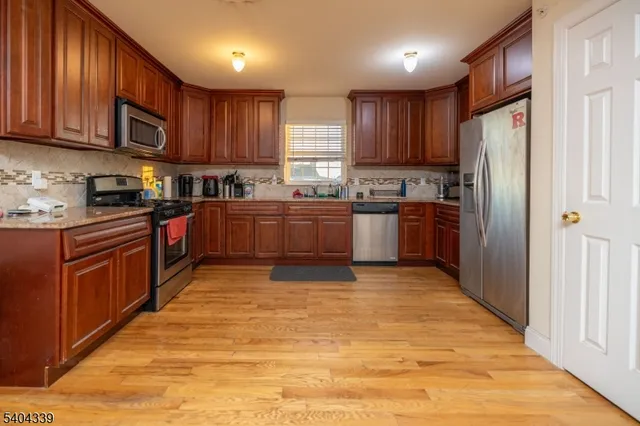 a kitchen with stainless steel appliances granite countertop a stove top oven a refrigerator a sink and dishwasher with wooden cabinets