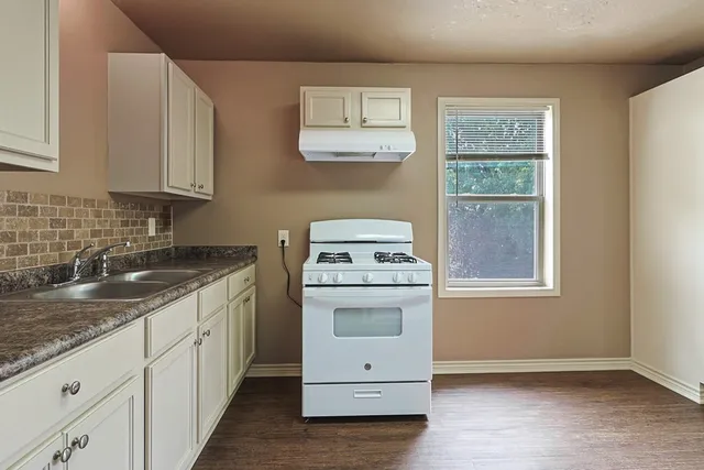 a kitchen with granite countertop white cabinets and a stove top oven