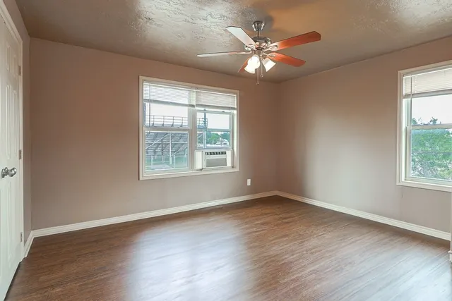 an empty room with wooden floor fan and windows