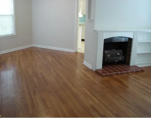 an empty room with wooden floor fireplace and windows