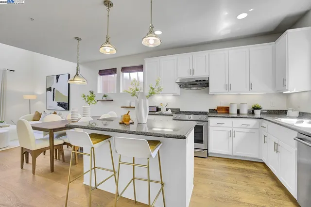 a kitchen with stainless steel appliances granite countertop a sink a stove a kitchen island with chairs and white cabinets