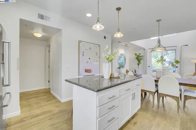 a dining hall with stainless steel appliances granite countertop furniture a sink a rug a chandelier and a view of living room