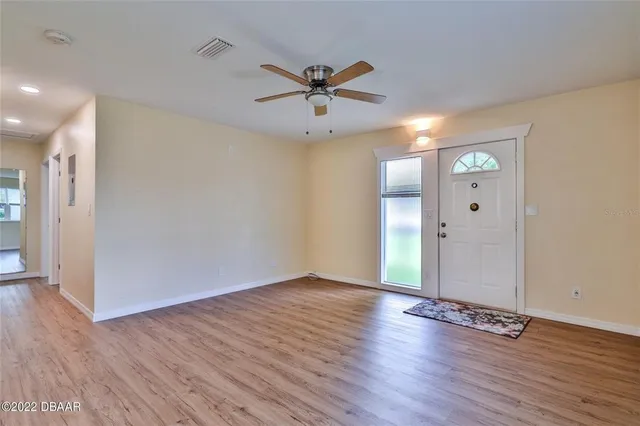 an empty room with wooden floor a ceiling fan and windows