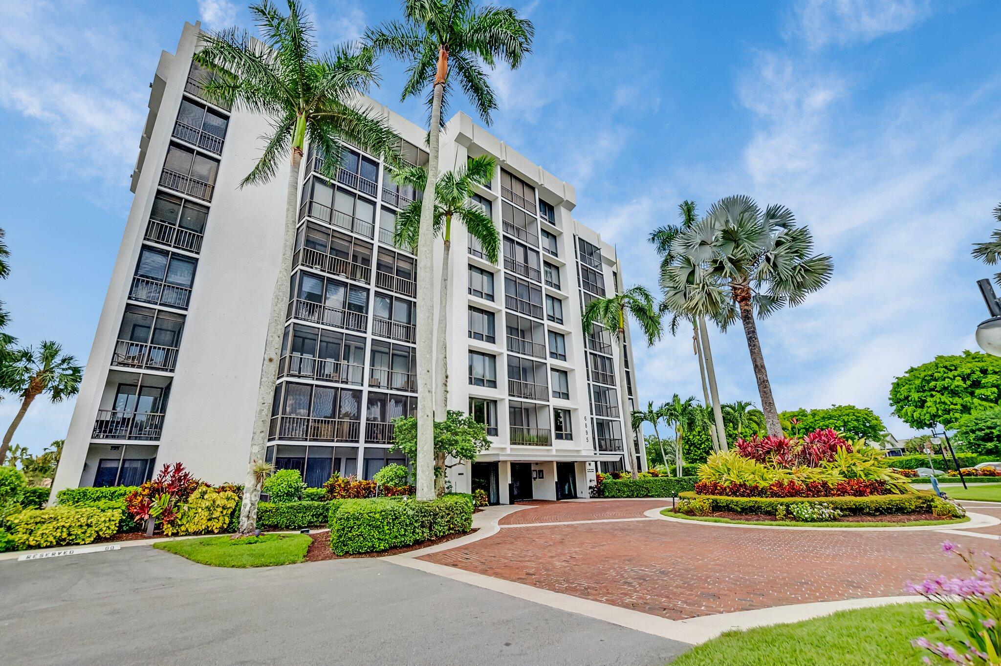 6895 Willow Wood Drive, Unit 1083 Boca Raton, FL 33434 - Photo 1 of 56 a front view of multi story residential apartment building with yard and flowers in it
