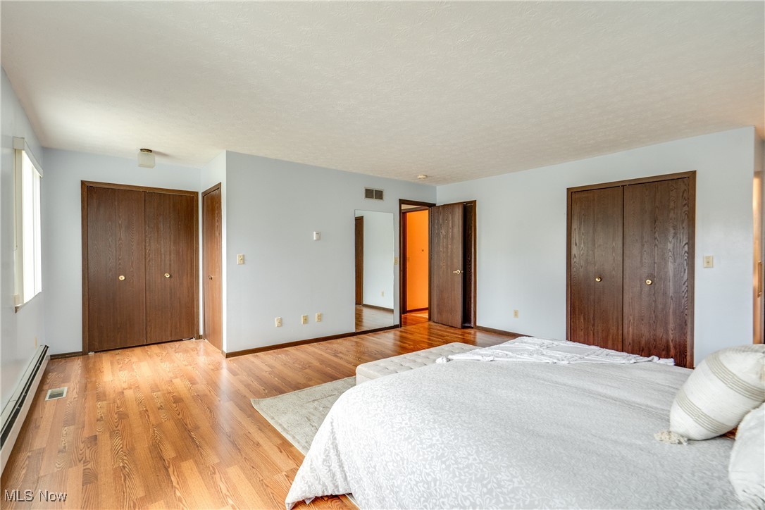 308 Guy's Run Road Akron, OH 44319 - Photo 26 of 44 Bedroom featuring a baseboard heating unit, multiple closets, visible vents, and light wood-type flooring