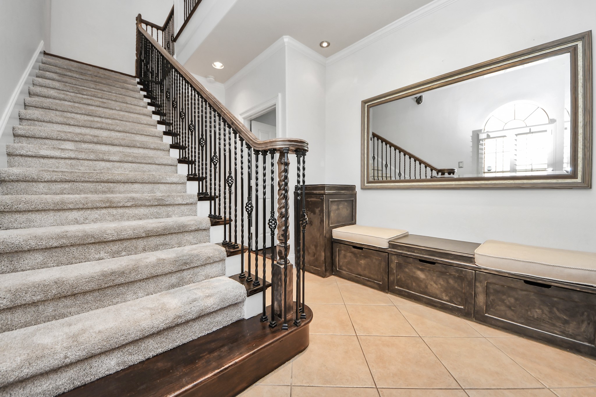 710 Jackson Hill Street Houston, TX 77007 - Photo 4 of 31 Welcoming entry and staircase with elegant wrought iron railing. A large mirror enhances the space, accompanied by a built-in bench with storage below, perfect for a stylish and functional entrance.