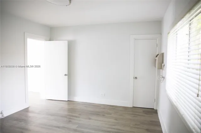 an empty room with wooden floor closet and windows