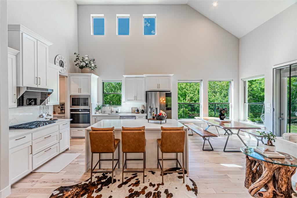 1070 Adair Road Prosper, TX 75078 - Photo 6 of 40 Open-concept kitchen and dining area featuring a vaulted ceiling, light wood-finish flooring, white cabinetry, a kitchen island with seating, and a built-in oven and microwave