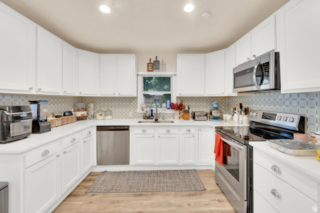 501 Canyon Road Ogden, UT 84404 - Photo 23 of 30 Kitchen featuring extensive white cabinetry, light countertops, wood-finish flooring, stainless steel appliances, and a tiled backsplash