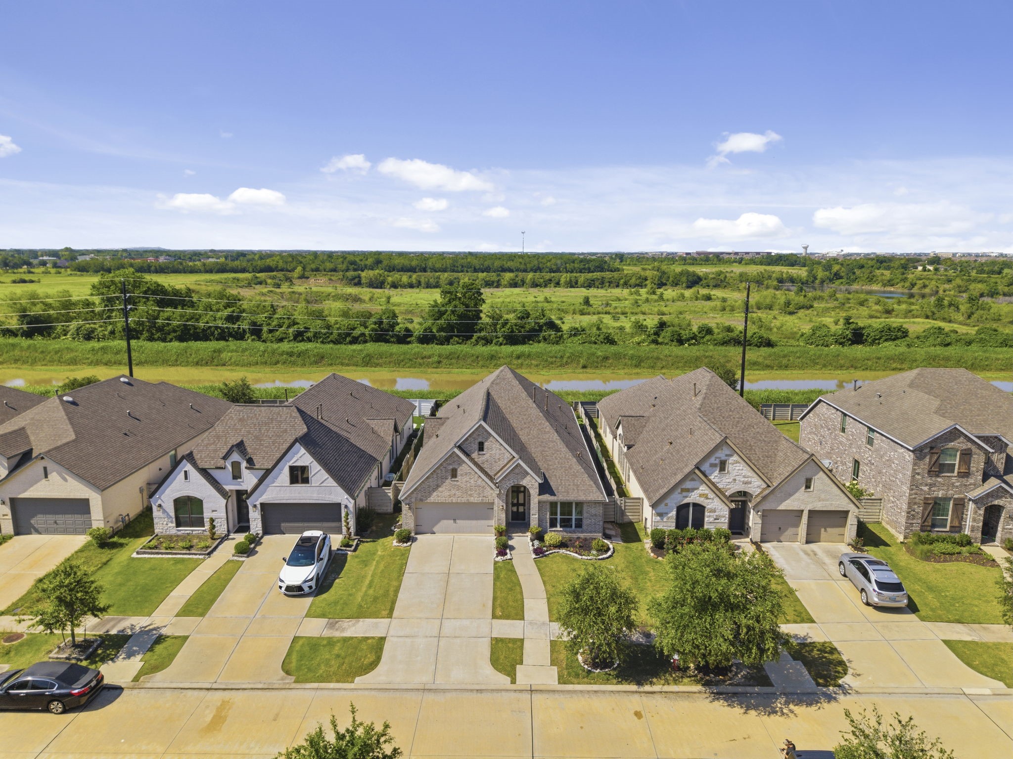 2119 Blackhawk Ridge Lane Manvel, TX 77578 - Photo 2 of 49 Stunning aerial view showcasing the home's beautiful brick and stone elevation, beautiful front landscaping, and wide concrete driveway. Notice the expansive open greenbelt and waterway directly behind the property — delivering the privacy and open views that come with having absolutely no back neighbors, a rare and highly sought-after feature in Pomona.