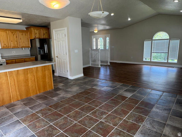 88 Canterbury Lane Logan, UT 84321 - Photo 15 of 37 Open-concept living space with vaulted ceilings, large arched window, wood-finish flooring, tile flooring, and a kitchen featuring wood cabinetry and an island with a countertop