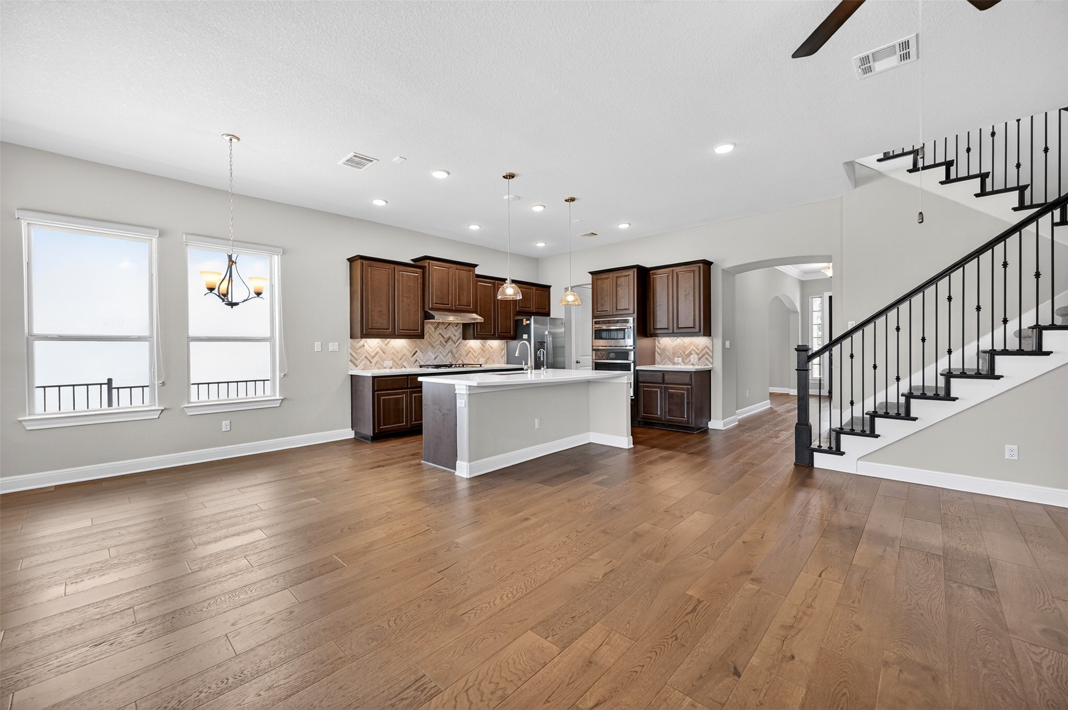 1201 Positano Pass Leander, TX 78641 - Photo 11 of 40 Open-concept interior featuring wood-finish flooring, a kitchen island with pendant lighting, dark wood cabinetry, and stainless steel appliances
