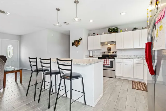 a kitchen with stainless steel appliances kitchen island granite countertop a refrigerator a stove and white cabinets with wooden floor