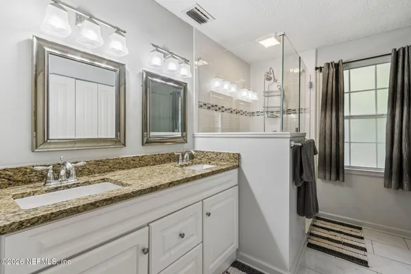 a bathroom with a granite countertop sink two mirror and a refrigerator