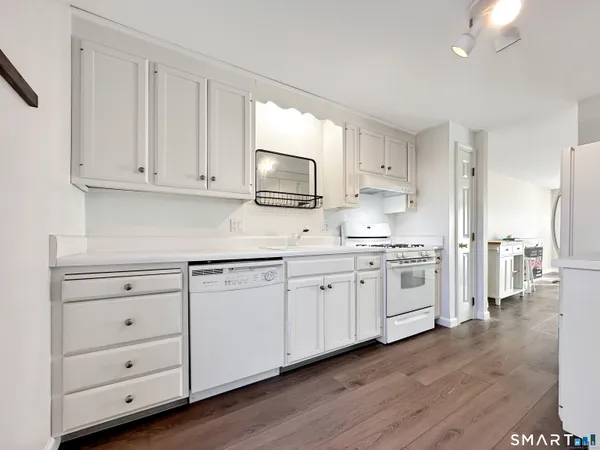 a kitchen with granite countertop white cabinets and white appliances with wooden floor