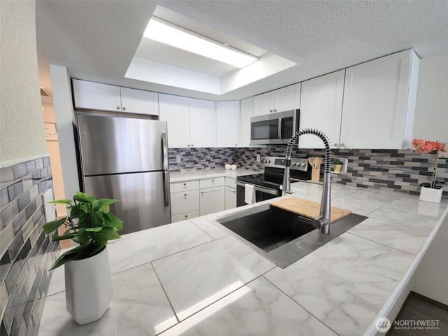 a kitchen with stainless steel appliances kitchen island granite countertop a refrigerator a stove a sink dishwasher and white cabinets with wooden floor
