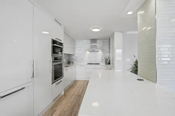 a large white kitchen with kitchen island a sink stainless steel appliances and cabinets