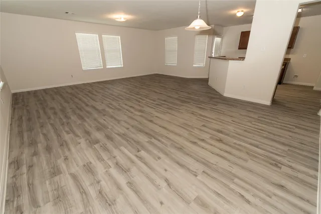 an empty room with wooden floor white walls and kitchen view