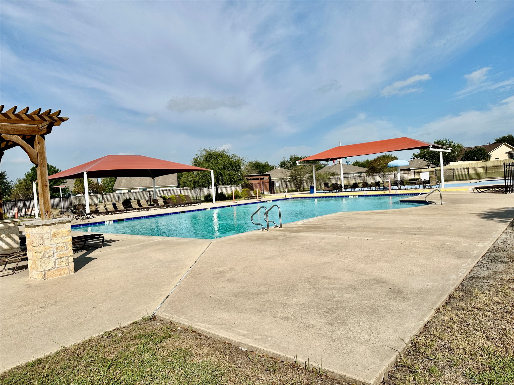 207 Dragon Ridge Road Buda, TX 78610 - Photo 31 of 38 Community pool featuring concrete decking, a large rectangular swimming area, and two red shade structures