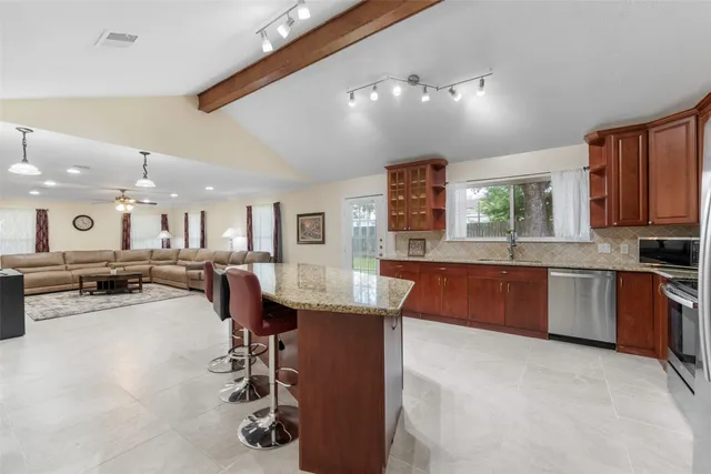 a kitchen with stainless steel appliances kitchen island granite countertop a sink dishwasher a stove a dining table and chairs with wooden floor