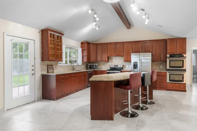 a kitchen with stainless steel appliances granite countertop a stove top oven a sink dishwasher a dining table and chairs with wooden floor