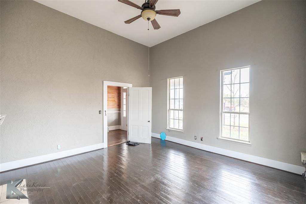 141 East 3rd Street Baird, TX 79504 - Photo 11 of 33 an empty room with wooden floor chandelier fan and windows
