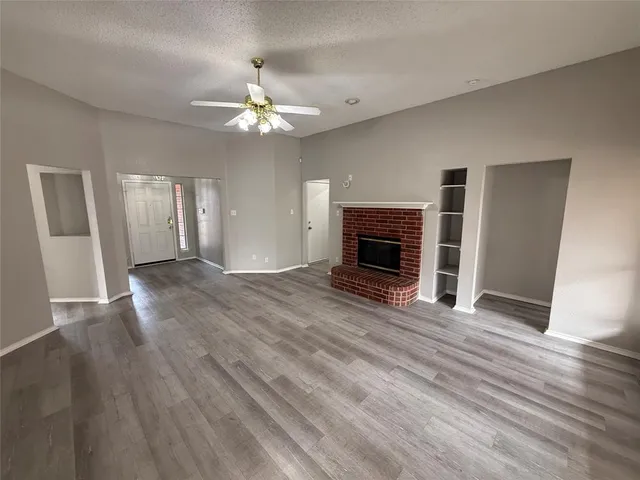a view of an empty room with wooden floor fireplace and a window