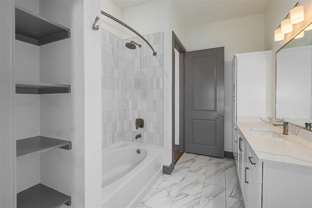 2700 Old Denton Road, Unit 1044 Carrollton, TX 75007 - Photo 6 of 33 Bathroom featuring a white bathtub with subway tile surround, built-in shelving, a vanity with a rectangular undermount sink and stone-finish countertop, and patterned tile flooring
