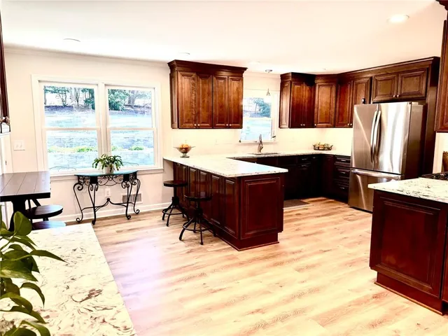 a living room with stainless steel appliances kitchen island granite countertop a refrigerator a sink dishwasher a dining table and chairs with wooden floor