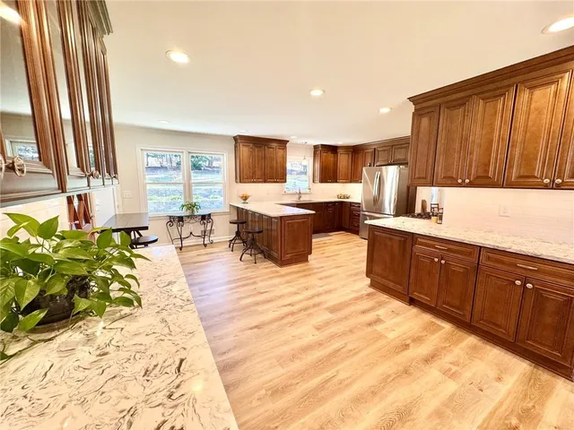 a kitchen with stainless steel appliances granite countertop a refrigerator a stove top oven and a sink with wooden floor