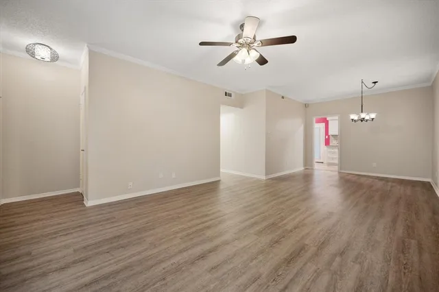 a view of an empty room with wooden floor and a ceiling fan