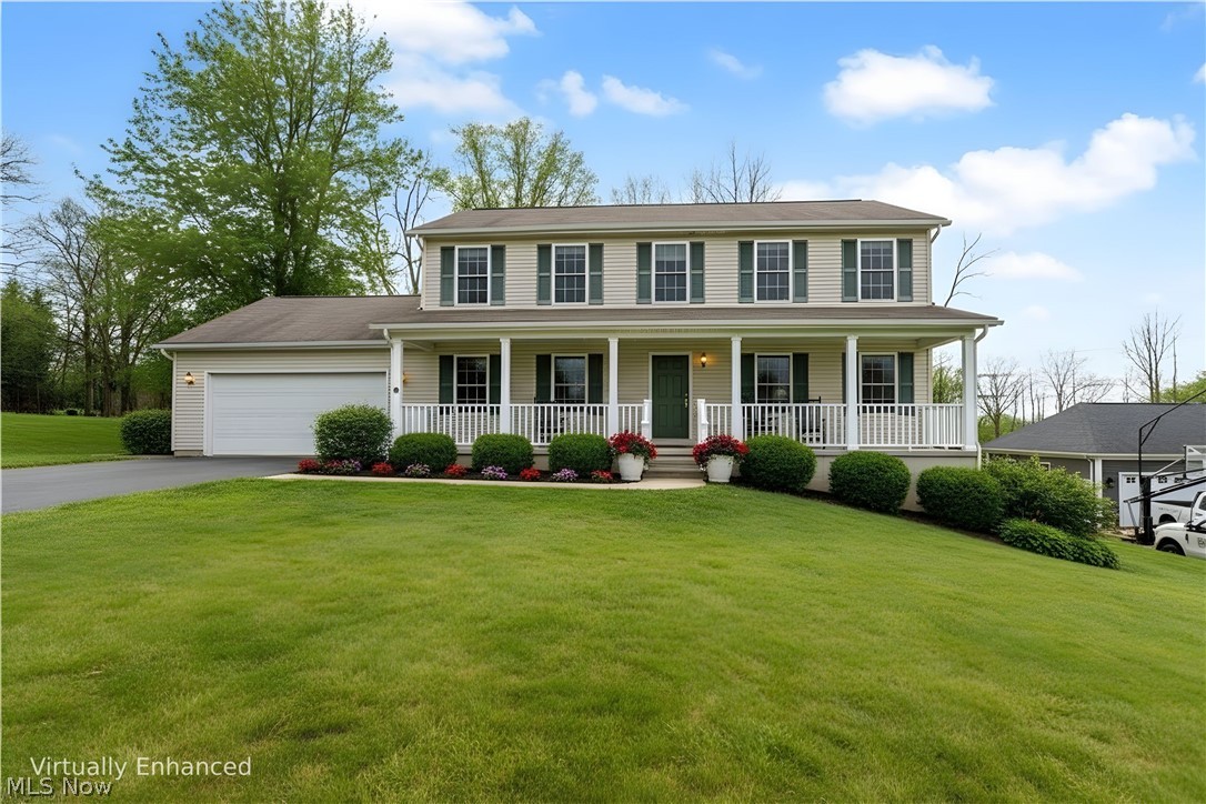 Colonial-style house featuring a porch, a front yard, an attached garage, and asphalt driveway