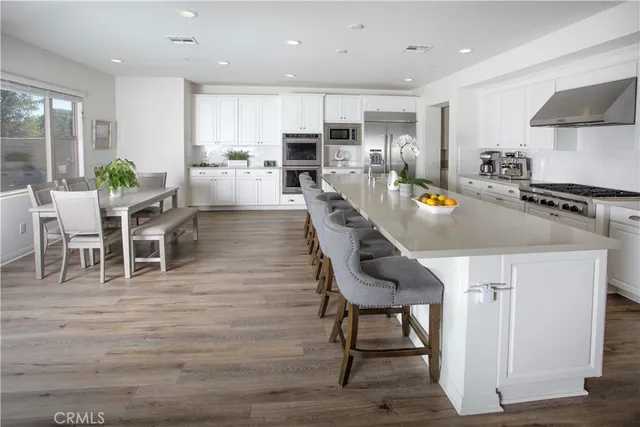 a kitchen with stainless steel appliances granite countertop a stove top oven a refrigerator a dining table and chairs with wooden floor