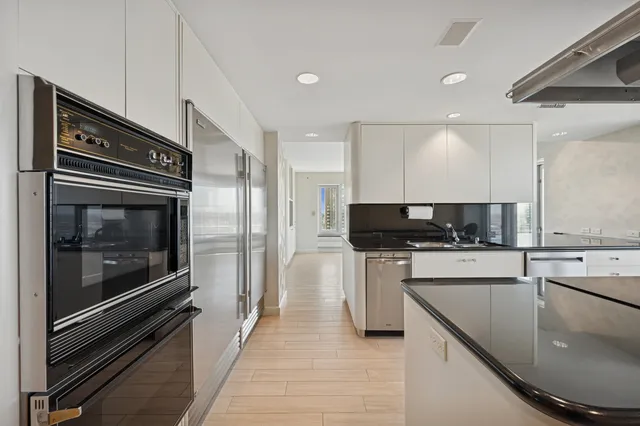 a large white kitchen with a sink and dishwasher a stove top oven with wooden floor