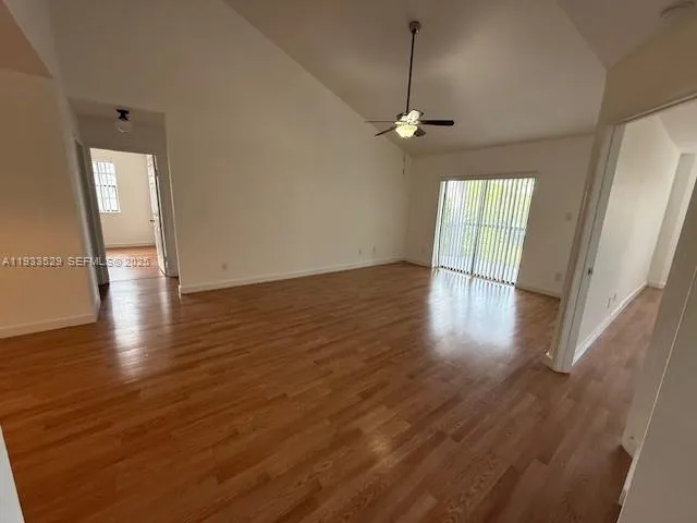 an empty room with wooden floor fan and windows