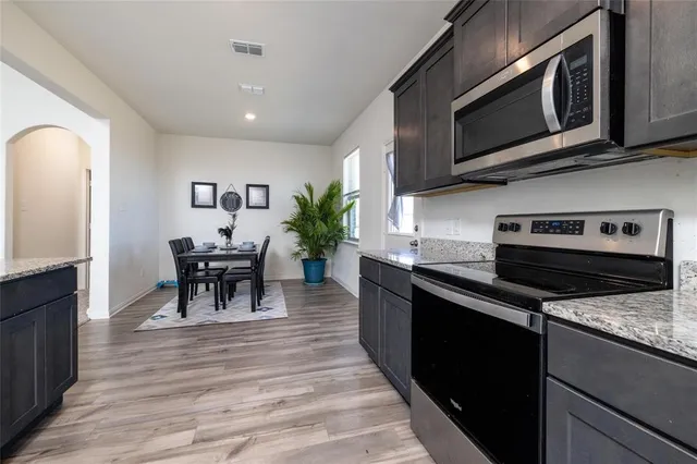 a kitchen with stainless steel appliances granite countertop a refrigerator a stove top oven a sink dishwasher and wooden cabinets with wooden floor