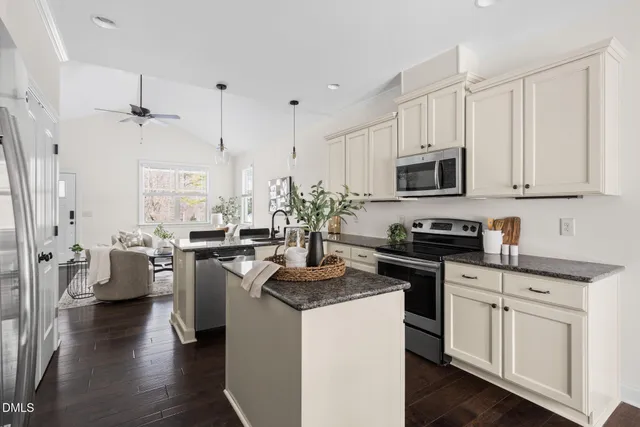 a kitchen with stainless steel appliances a stove a sink dishwasher a microwave oven with white cabinets and wooden floor